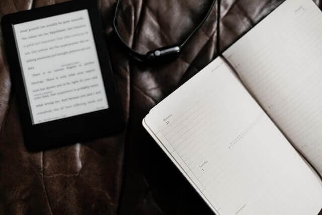 a Kindle together with a notebook placed on a leather sofa